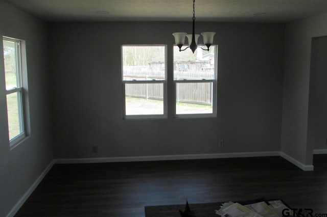 unfurnished dining area with dark wood-type flooring, baseboards, and an inviting chandelier