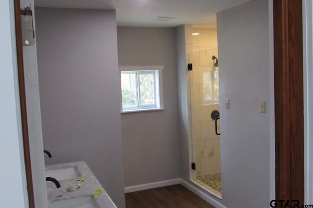 full bath featuring double vanity, wood finished floors, a shower stall, and baseboards