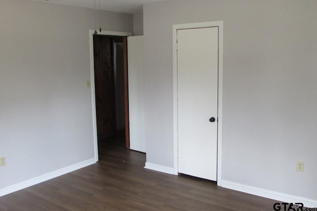 unfurnished bedroom featuring dark wood-type flooring, a closet, and baseboards