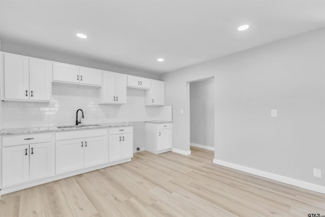 kitchen featuring light wood-type flooring, white cabinets, decorative backsplash, and a sink