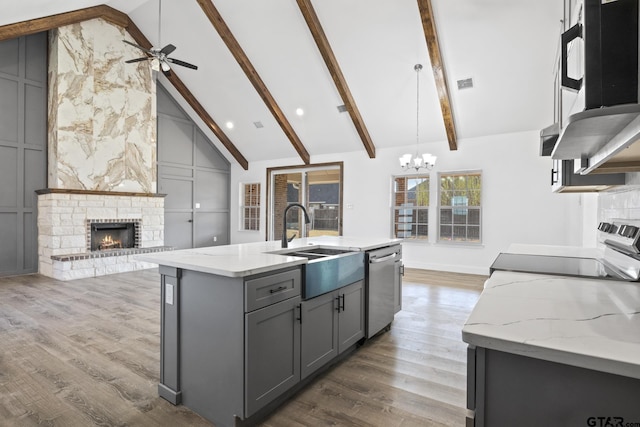 kitchen with dark wood-type flooring, a stone fireplace, stainless steel dishwasher, an island with sink, and gray cabinets