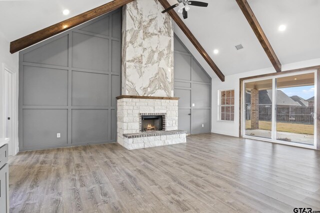 unfurnished living room with beam ceiling, light hardwood / wood-style flooring, ceiling fan, and a stone fireplace