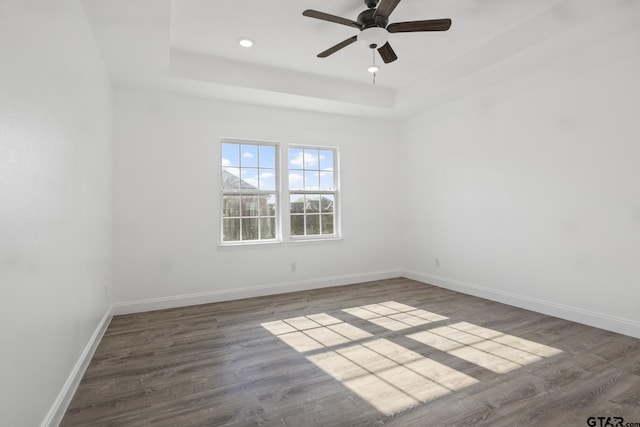 unfurnished room with dark hardwood / wood-style flooring, a tray ceiling, and ceiling fan