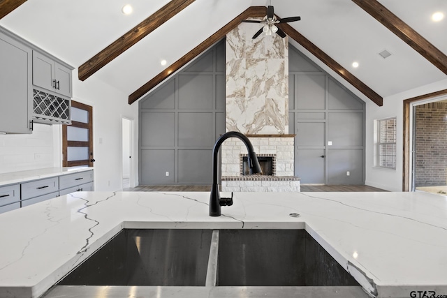 kitchen featuring vaulted ceiling with beams, light stone countertops, and gray cabinets