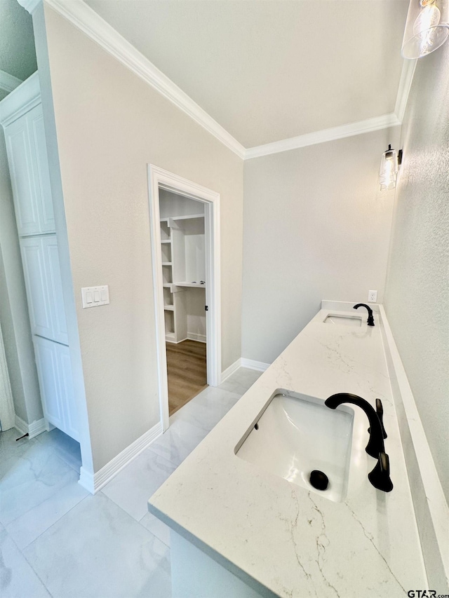 full bathroom featuring double vanity, baseboards, ornamental molding, and a sink
