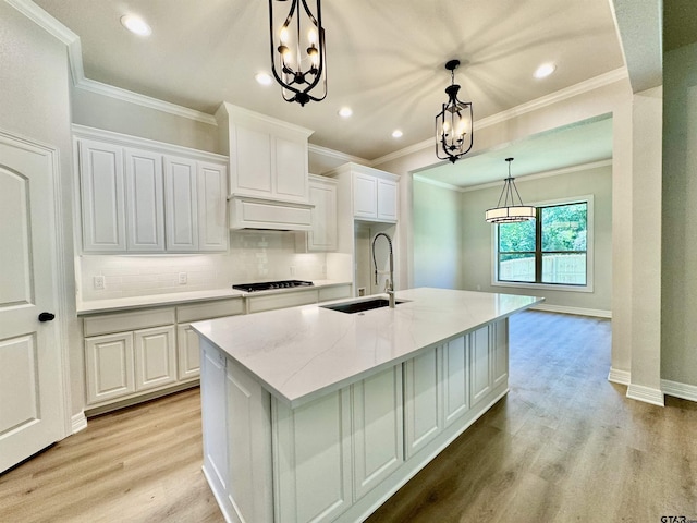 kitchen with a sink, an inviting chandelier, light wood finished floors, white cabinets, and cooktop