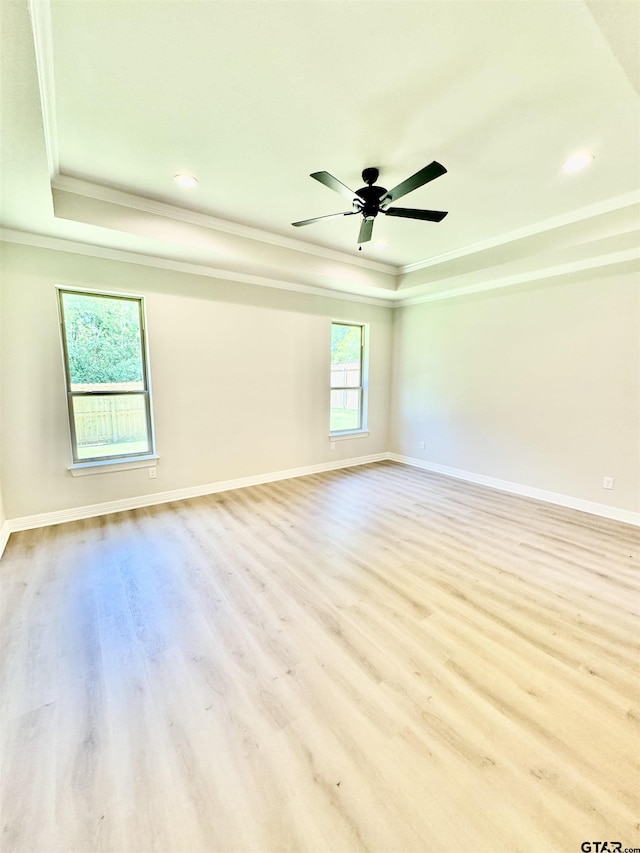 empty room with a tray ceiling, ornamental molding, and wood finished floors