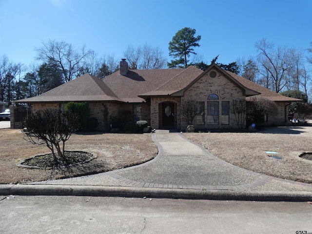 french country inspired facade with roof with shingles, brick siding, and a chimney