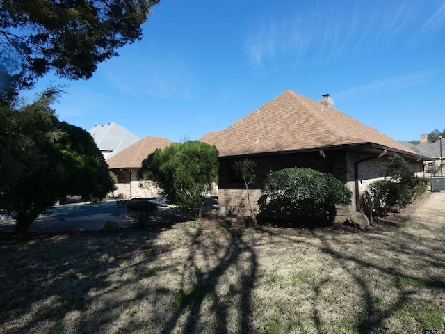 view of property exterior with a yard, a shingled roof, a chimney, and central air condition unit