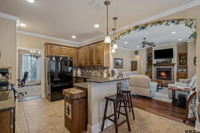 kitchen featuring arched walkways, visible vents, open floor plan, dark stone countertops, and black fridge