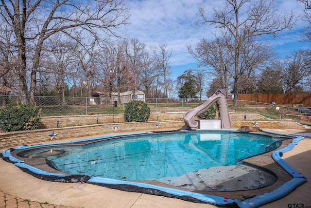 view of swimming pool with a fenced in pool, an outbuilding, a storage shed, a water slide, and a fenced backyard