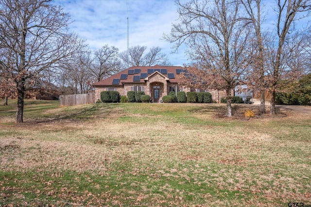 view of front of home featuring stone siding, a front yard, roof mounted solar panels, and fence