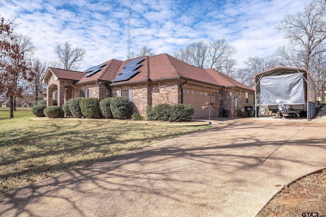 view of side of home featuring a garage, driveway, a yard, roof mounted solar panels, and brick siding