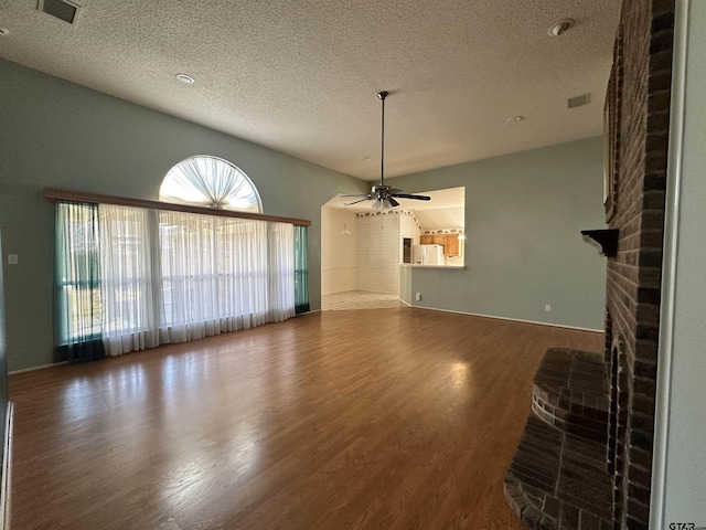 unfurnished living room featuring a brick fireplace, hardwood / wood-style flooring, a textured ceiling, and ceiling fan