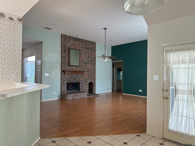 unfurnished living room with light hardwood / wood-style floors, a brick fireplace, and a textured ceiling