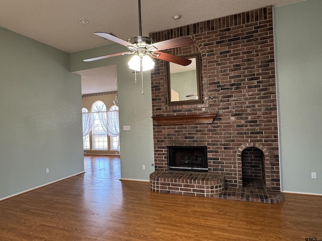 unfurnished living room with ceiling fan, hardwood / wood-style floors, a brick fireplace, and a textured ceiling