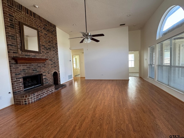 2414 Stillwater Dr, Mesquite, TX 75181 - unfurnished living room featuring a brick fireplace, wood finished floors, a textured ceiling, ceiling fan, and a towering ceiling