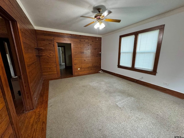 empty room with dark carpet, crown molding, a textured ceiling, wooden walls, and ceiling fan