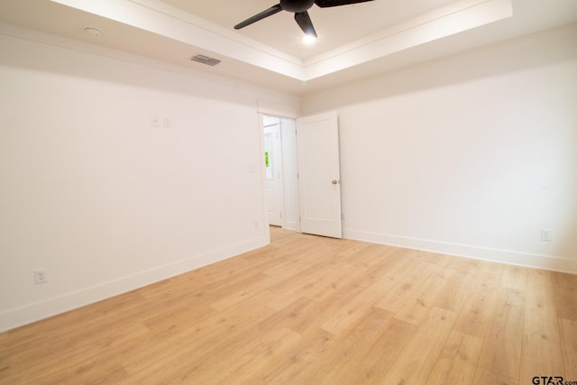 empty room with ceiling fan, light hardwood / wood-style floors, and a tray ceiling