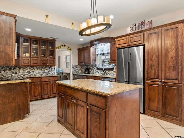 kitchen featuring a center island, hanging light fixtures, stainless steel refrigerator, light stone counters, and light tile patterned flooring