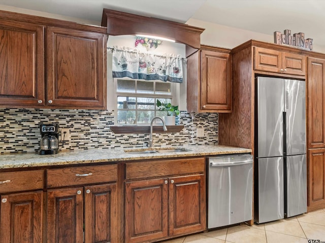 kitchen featuring appliances with stainless steel finishes, light stone countertops, light tile patterned flooring, backsplash, and sink