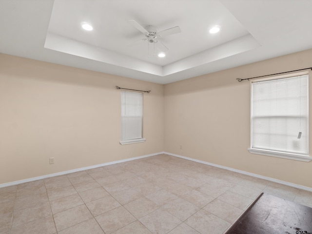 empty room featuring ceiling fan, a raised ceiling, and a wealth of natural light