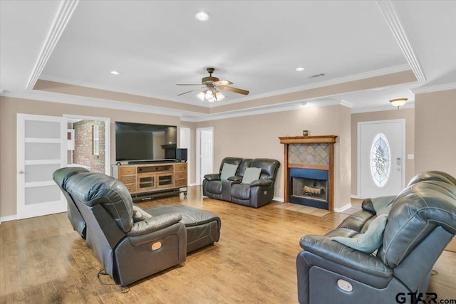 living room featuring ornamental molding, ceiling fan, a tile fireplace, and light hardwood / wood-style floors