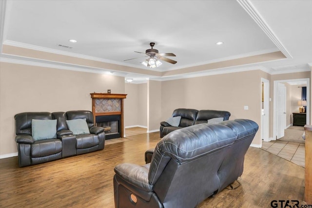 living room with crown molding, a tiled fireplace, hardwood / wood-style flooring, a tray ceiling, and ceiling fan