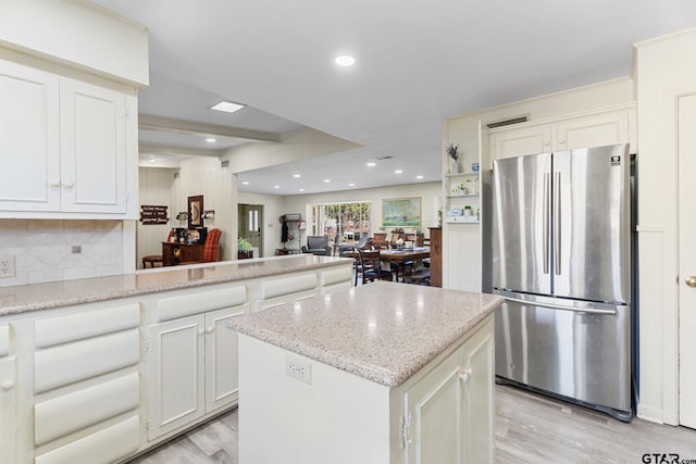 kitchen with stainless steel fridge, white cabinetry, a center island, light stone countertops, and light wood-type flooring