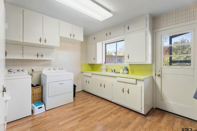 laundry area featuring washing machine and clothes dryer, a healthy amount of sunlight, sink, and light hardwood / wood-style floors