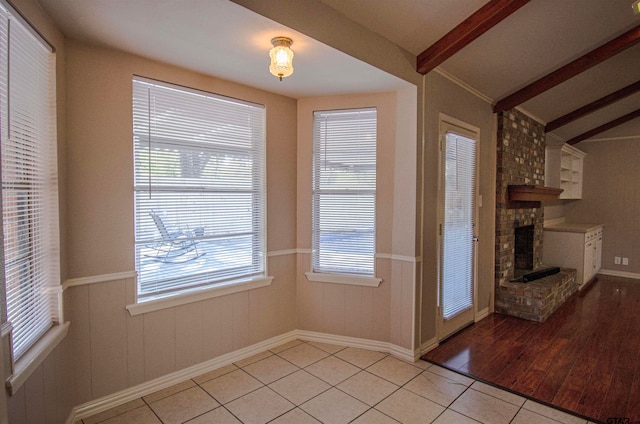 doorway featuring a brick fireplace, a healthy amount of sunlight, light hardwood / wood-style flooring, and lofted ceiling with beams