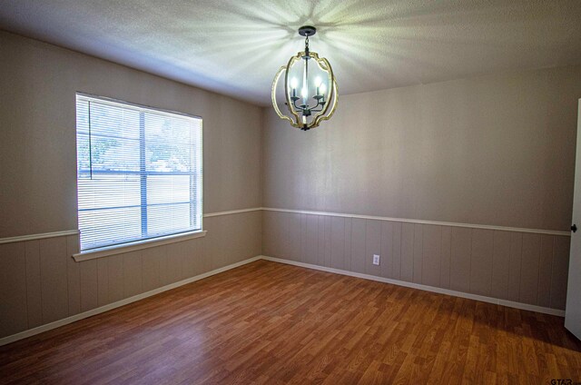 spare room with wood-type flooring, a textured ceiling, and a notable chandelier