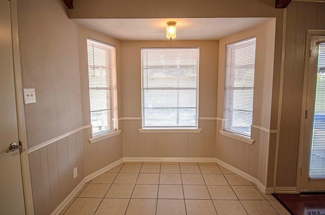 unfurnished dining area with wood walls, light tile patterned floors, and plenty of natural light