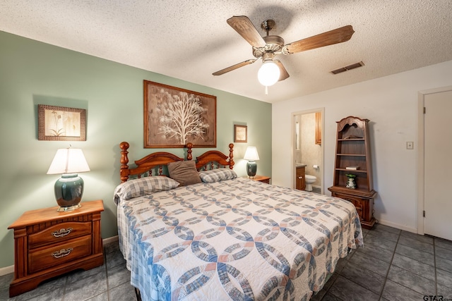 bedroom with a textured ceiling, ensuite bathroom, ceiling fan, and dark tile patterned floors