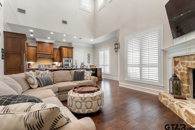 living room featuring a high ceiling, dark wood-type flooring, ornamental molding, and a fireplace