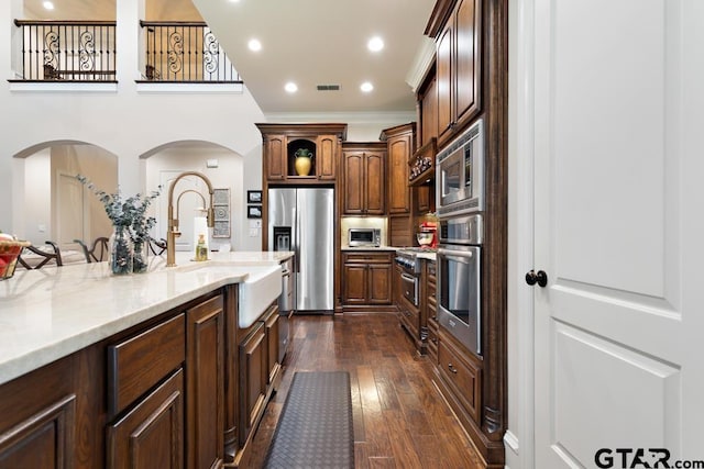 kitchen featuring sink, light stone counters, appliances with stainless steel finishes, ornamental molding, and dark hardwood / wood-style flooring