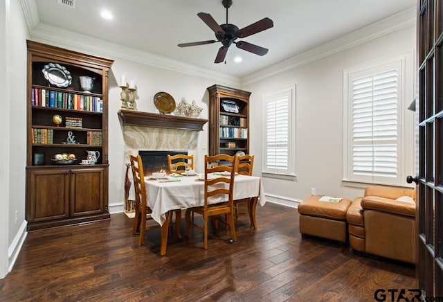 dining space with dark wood-type flooring, ceiling fan, crown molding, and a high end fireplace