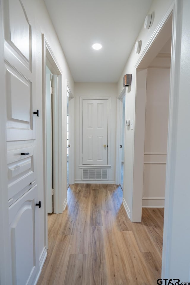 hall with light wood finished floors, visible vents, and baseboards