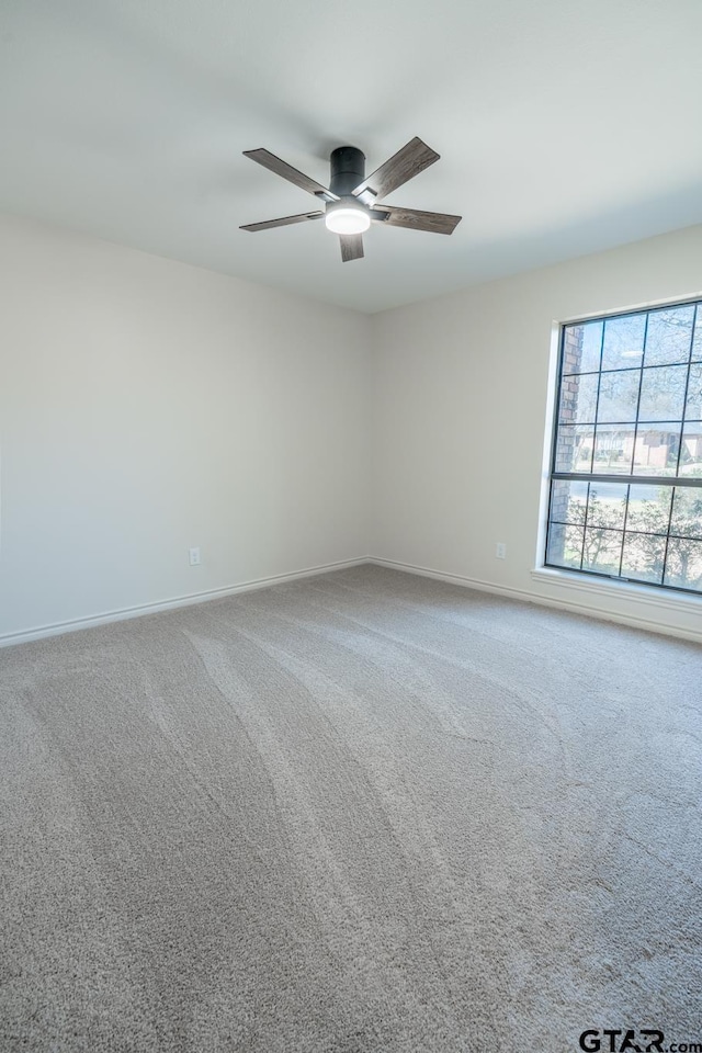 carpeted spare room featuring baseboards and a ceiling fan