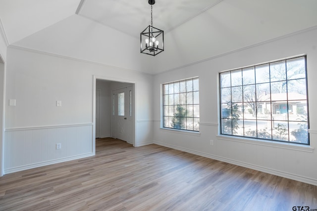 spare room with lofted ceiling, a wainscoted wall, light wood-type flooring, and a notable chandelier