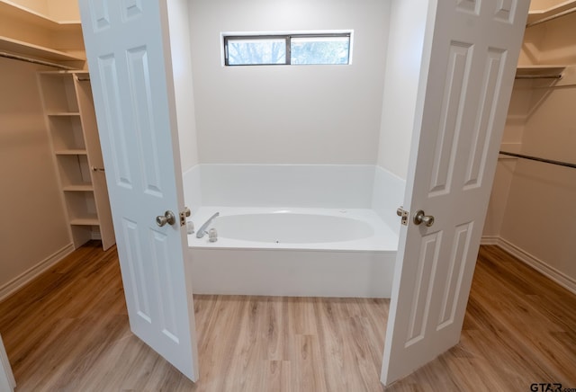 bathroom featuring a walk in closet, a garden tub, and wood finished floors