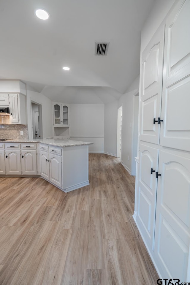 kitchen featuring visible vents, light wood-style floors, white cabinetry, decorative backsplash, and range hood