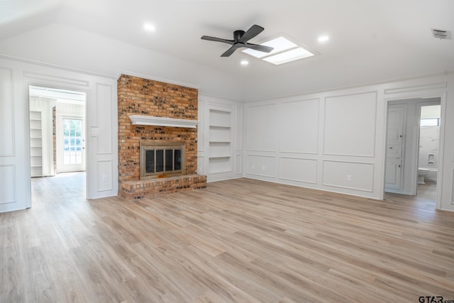 unfurnished living room with built in shelves, a brick fireplace, a decorative wall, and light wood finished floors