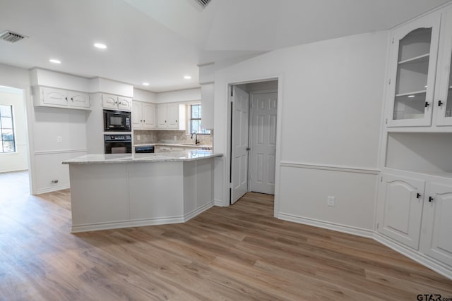 kitchen featuring visible vents, light wood-style floors, a peninsula, black appliances, and a sink