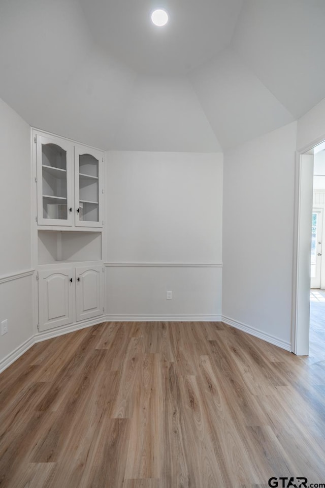 spare room with lofted ceiling, light wood-style flooring, and baseboards