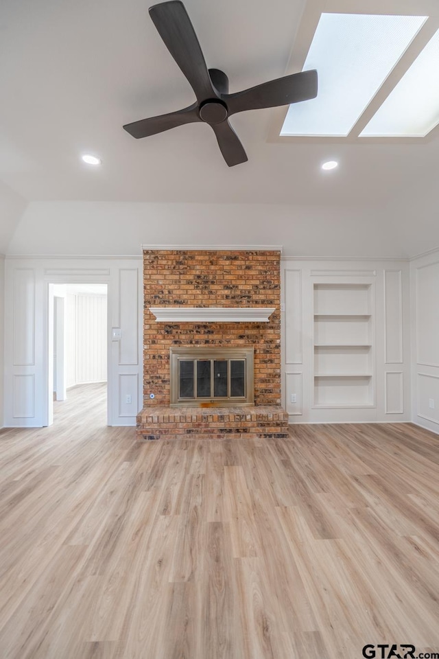 unfurnished living room featuring built in shelves, a fireplace, a decorative wall, ceiling fan, and wood finished floors