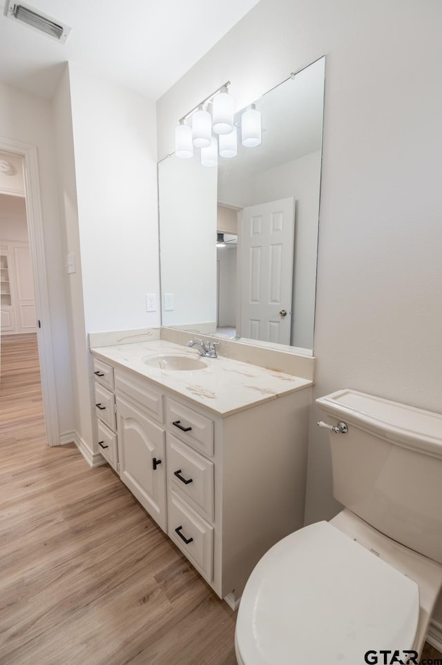 bathroom with toilet, vanity, wood finished floors, and visible vents