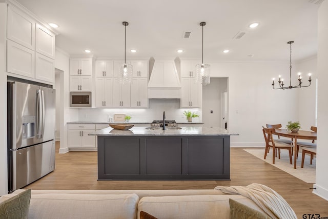 kitchen featuring premium range hood, pendant lighting, built in microwave, white cabinetry, and stainless steel fridge