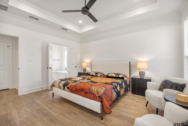 bedroom featuring connected bathroom, crown molding, light wood-type flooring, a tray ceiling, and ceiling fan