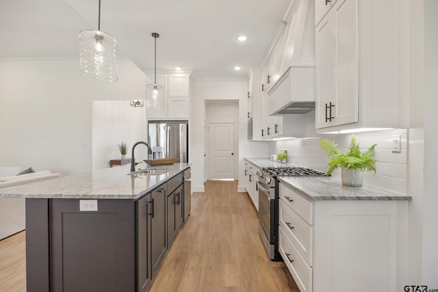 kitchen with appliances with stainless steel finishes, decorative light fixtures, white cabinetry, sink, and a kitchen island with sink